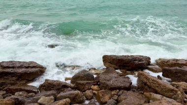 Sakin bir sahil şeridi boyunca kayalık oluşumlara çarpan dalgaların nefes kesici güzelliğini hissedin.