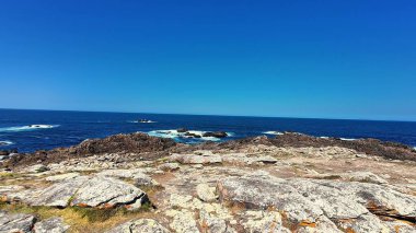 Çarpıcı bir manzara engebeli bir kıyı şeridinin berrak, güzel gökyüzünün altında dingin mavi bir okyanusla birleşmesini gösteriyor.