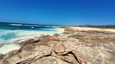Engebeli kayalık sahilin şaşırtıcı güzellikteki manzarasında berrak mavi gökyüzü ve okyanus dalgaları çarpışıyor.