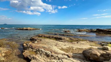 Parlak, güneşli bir gökyüzünün altında engebeli kıyı şeridinin berrak mavi okyanusla buluşmasının tadını çıkar.