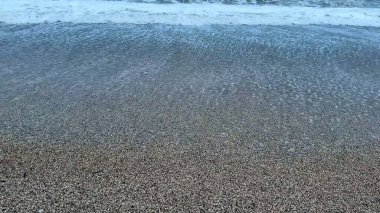 Sakin okyanus dalgaları, alacakaranlıkta pürüzsüz bir çakıl taşının üzerinde süzülüp huzurlu ve huzurlu bir atmosfer yaratıyor.