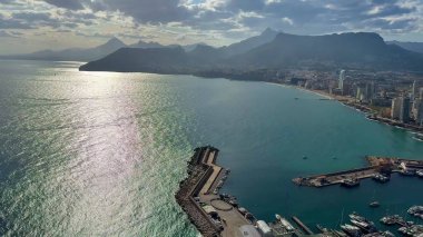 Sersemletici hava manzarası kıyı şehrini, dağları ve bulutlu gökyüzünün altında canlı marinayı gösteriyor..