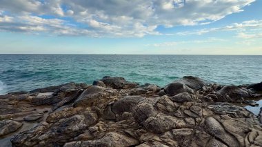 Üzerinde yumuşak, bulutlu bir gökyüzü altında kayalık çıkıntılar barındıran güzel, sakin bir kıyı manzarası.