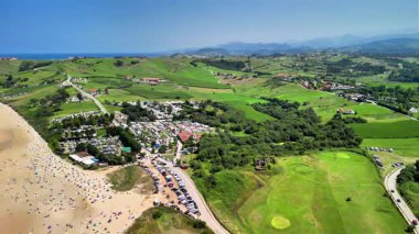 Bu çarpıcı hava manzarası bereketli tepeler ve büyüleyici kıyı manzarasıyla çevrili hareketli bir plajı gösteriyor.