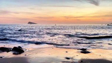 Gün batımında güzel ve sakin bir sahil sahnesi. Yumuşak dalgalar sergileniyor. Kayalık bir sahil şeridinde rahatlamak için mükemmel.