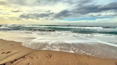 Huzurlu sahil dalgalarının dinginliğini hisset dramatik ve bulutlu bir gökyüzünün altında yavaşça yuvarlan