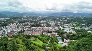 Arka planda görkemli dağlar tarafından çerçevelenmiş canlı bir kıyı şehrinin çarpıcı bir hava manzarasını deneyimleyin.