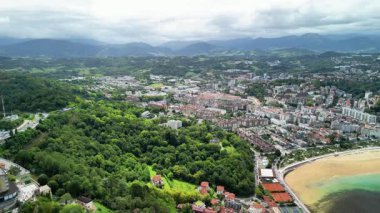 Görkemli dağlarla barışçıl plajlar arasına kurulmuş canlı bir sahil kasabasını gösteren çarpıcı bir hava fotoğrafı.