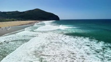 Çarpıcı bir sahil manzarası, canlı dalgalar nazikçe çarpıyor, ve açık mavi gökyüzü, yaz rahatlığı için mükemmel.