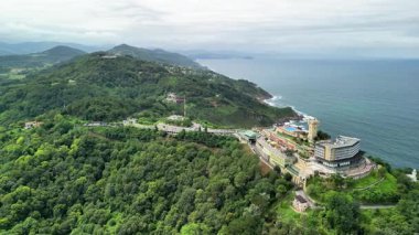 Havadan çekilen görüntüler, gür, yeşil tepelerin arasına yerleştirilmiş, parlak okyanus dalgalarının yanında nefes kesici bir sahil beldesi yakalıyor.