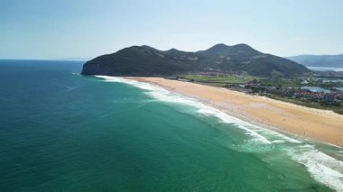 Görkemli dağlar ve canlı turkuaz sularla çevrili altın plajın çarpıcı hava manzarası.