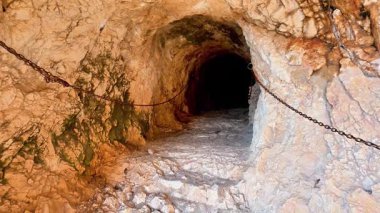 Loş ışıklı bir mağara tünelinin büyüleyici ve büyüleyici görüntüsü, güvenlik için eşsiz kaya dokuları ve zincirleri barındırıyor.