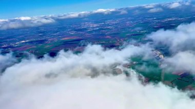 Sersemletici hava görüntüleri parlak mavi gökyüzünün altında geniş yeşil alanlar ve kabarık bulutlar sergiliyor.