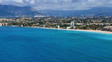 Canlı bir kıyı şeridinin dingin mavi gökyüzünün altında turkuaz sularla buluştuğu nefes kesici hava manzarasını deneyin.