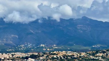 Büyüleyici evlerin üzerinde dramatik bulutlar olan görkemli dağların çarpıcı manzarası.
