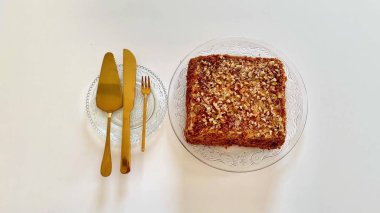 İnanılmaz cezbedici kare bir tatlı, el değmemiş beyaz bir yüzey üzerinde parlak altın kaplar ile zarif bir şekilde sunulur.