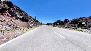 Kayalık volkanik arazi ve açık mavi gökyüzüyle çevrili sarmal asfalt bir yolun çarpıcı manzarası.