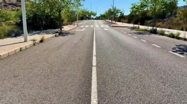 Açık mavi gökyüzünün altında ağaçlarla kaplı, uzun ve ıssız bir köy yolunun resimsel manzarası.