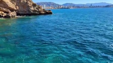 Nefes kesen kıyı manzaraları berrak mavi suları sergiliyor, kayalık uçurumlar, hepsi güneşli bir gökyüzünün altında.