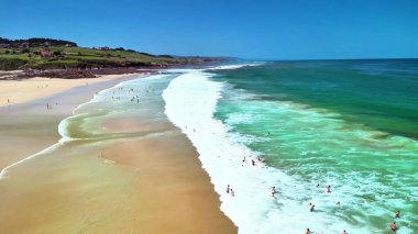 Heyecanlı sörfçülerin, el değmemiş turkuaz suların ve güneşli altın kumların sergilendiği nefes kesici bir plaj sahnesi.