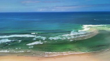 Okyanus dalgalarının, berrak, parlak mavi bir gökyüzünün altında kumlu bir sahile nazikçe uzanan muhteşem sakin manzarası.