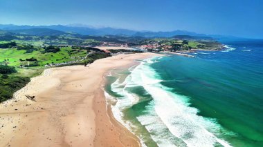Nefes kesici bir hava görüntüsü, berrak mavi gökyüzünün altındaki çarpıcı sahili ve canlı manzarayı yakalar.