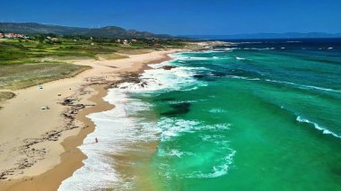 Canlı zümrüt suları ve kayalık bir sahil şeridine sahip güzel, el değmemiş bir plajı gösteren nefes kesici hava görüntüleri.