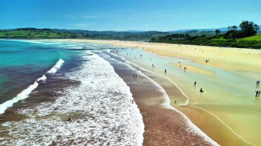 Güneş banyosu ve yumuşak dalgalarla dolu canlı, canlı bir plajı gösteren nefes kesici bir hava manzarası.