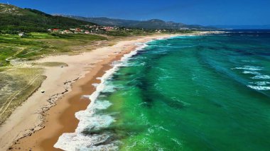 Havadan bakıldığında, turkuaz suları ve kıyıda hafif dalgaları olan el değmemiş bir sahil görünüyor.