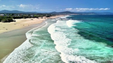 Serin ve berrak suları ve parlak gökyüzünün altında hafif dalgaları gösteren serin bir sahilin çarpıcı hava manzarası..