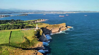 Hava manzarası, mükemmel güneşli bir günde sakin okyanus sularına bakan kayalıklarda çarpıcı bir deniz feneri gösteriyor.