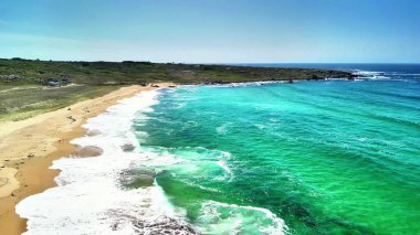Temiz turkuaz suları ve yumuşak dalgaları olan bozulmamış bir plajın nefes kesici hava manzarası.