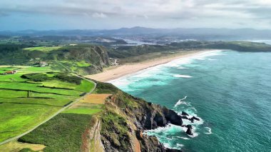 Canlı okyanus dalgaları ve yemyeşil tarlalarla bezenmiş pitoresk bir kıyı şeridini gösteren nefes kesici bir hava manzarası.