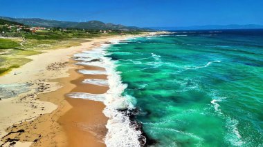 Huzurlu bir plajın çarpıcı manzarası altın kum ve kıyı boyunca dalgalanan canlı okyanus dalgalarıyla işaretlenmiştir.