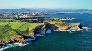 Resimli kıyı manzarası muhteşem bir deniz feneri, yüksek uçurumlar ve canlı yeşil alanlar içerir.