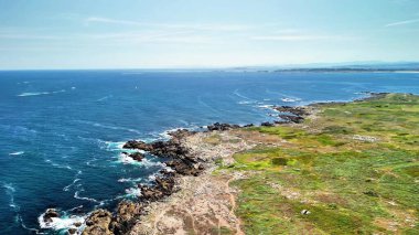 Engebeli kayalık kıyı şeritlerinin nefes kesici ve çarpıcı manzarası güneşli bir gökyüzünün altında berrak mavi sularla güzel bir şekilde buluşuyor.