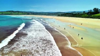 Güneş banyosu ve yumuşak dalgalarla dolu canlı, canlı bir plajı gösteren nefes kesici bir hava manzarası.