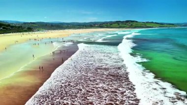 Temiz mavi suları, yumuşak altın kumları olan güzel bir sahil ve sıcak güneşin ve sörfün tadını çıkaran insanlar.
