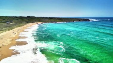 Temiz turkuaz suları ve yumuşak dalgaları olan bozulmamış bir plajın nefes kesici hava manzarası.