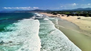 Dalgalar, altın kumlar ve açık mavi gökyüzüyle nefes kesici kumsal manzaralarının tadını çıkar.