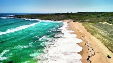 Canlı turkuaz dalgalar ve yumuşak altın kumlarla bezenmiş sakin bir sahili yakalayan çarpıcı bir hava manzarası.