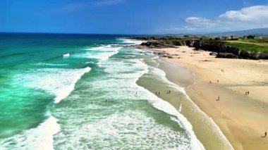 Nefes kesen kıyı manzaraları dalgaları, yumuşak kumları ve ufukta canlı mavi gökyüzünü gösteriyor.