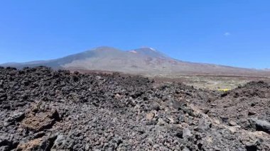 Olağanüstü volkanik kaya oluşumlarının nefes kesici manzaraları ve parlak mavi gökyüzünün altında yükselen bir volkan.