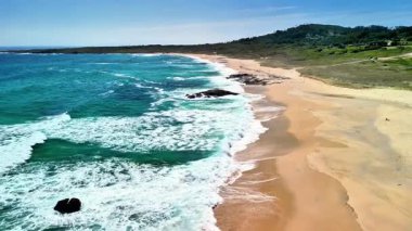 Kesinlikle çarpıcı bir hava fotoğrafında canlı dalgaları ve açık mavi gökyüzü olan güzel ve sakin bir plaj sergileniyor.