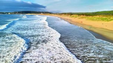 Dalgaların kumlu bir sahile çarpması, insanların mutlu bir şekilde güneşin tadını çıkarması ve okyanusun tazelenmesi.