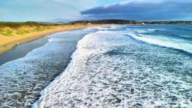 Sersemletici bir günbatımında kumlu sahilde süzülen okyanus dalgalarının sakin manzarası güzellikleri gözler önüne seriyor.