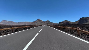 Berrak mavi gökyüzünün altında volkanik kayalar ve dağlarla çevrili açık bir yolun nefes kesici manzarası..