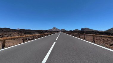 Berrak mavi gökyüzünün altında eşsiz bir volkanik manzara boyunca uzanan dolambaçlı bir yolun nefes kesici bir görüntüsü.