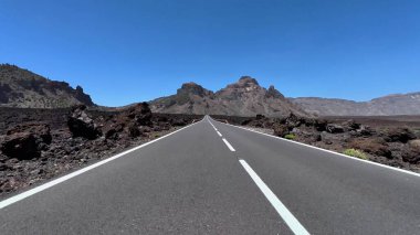 Dramatik volkanik arazi ve yukarıdaki güzel açık mavi gökyüzü ile çevrili nefes kesici bir yol manzarası.