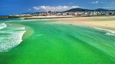 Berrak turkuaz suları, yumuşak altın kumları ve parlak, bulutsuz mavi gökyüzü ile çarpıcı bir kıyı şeridi.